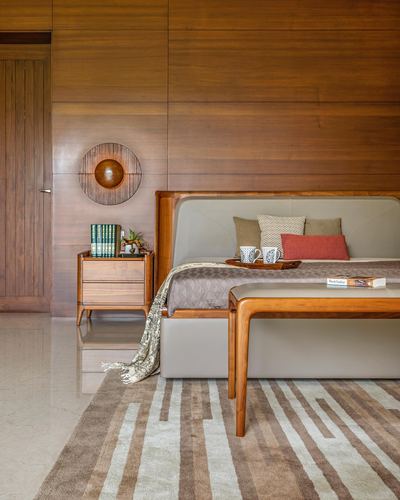 Wood-paneled bedroom with grey upholstered bed, wooden bench, and geometric rug