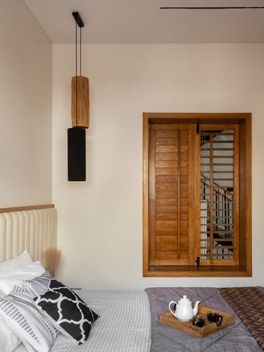 Bedroom with cylindrical wood pendant light beside a wooden shuttered window revealing a spiral staircase