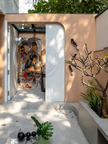 Arched white entrance door frames a colorful mural inside a terracotta-plastered courtyard facade with a bare tree.