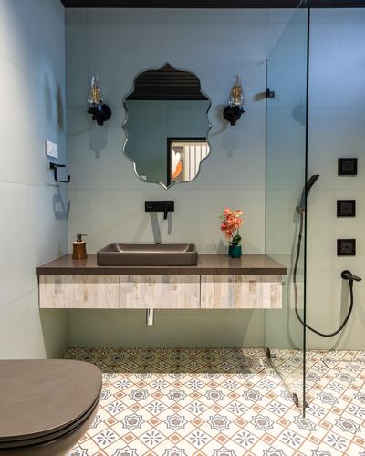Bathroom vanity with arched black-framed mirror, vessel sink, wood-front cabinetry, and patterned floor tiles