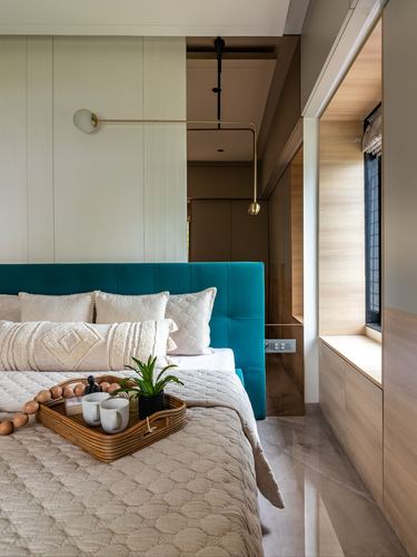 Teal velvet headboard bed with breakfast tray, brass wall lamp, and wooden window seat beyond