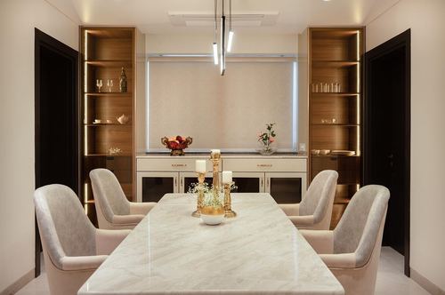 Symmetrical dining room with marble table, upholstered chairs, and backlit wood display shelving