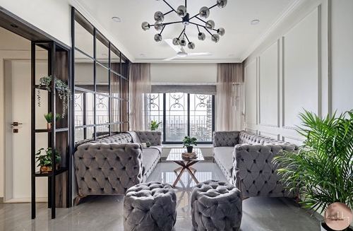 Symmetrical living room with grey tufted sofas, ottomans, chandelier, and city view through arched windows