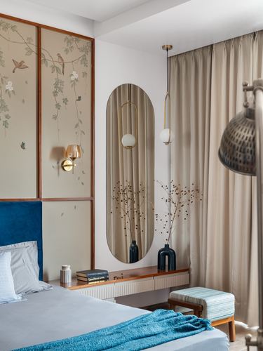 Bedroom with blue velvet headboard, floral wallpaper panel, and oval mirror above dresser