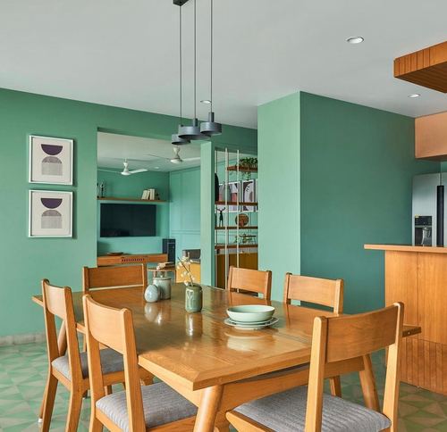 Green dining room with wooden table, chairs, and layered pendant lights