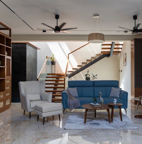 Living room with blue sofa, wingback chair, and floating wooden staircase under skylight