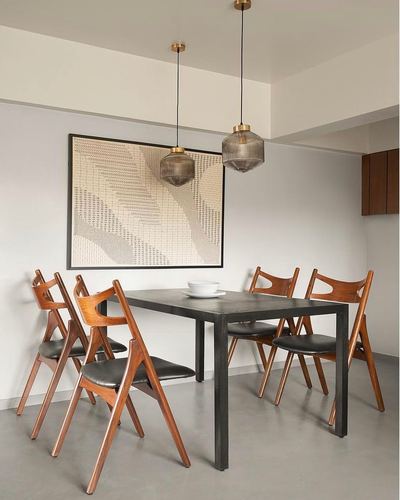 Dining area with black metal table, wooden scissor chairs, two smoked pendant lights, textile artwork