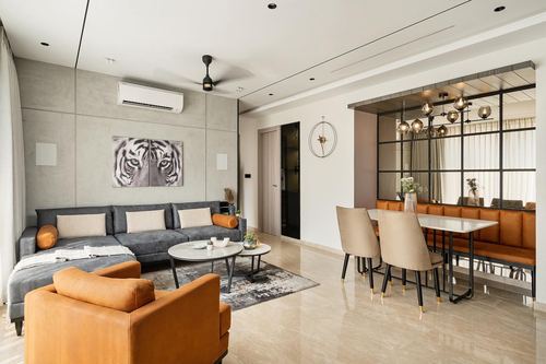 Open living and dining area with grey sectional, orange leather chair, and glass-partitioned dining nook