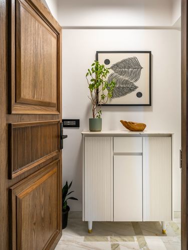 Entryway with open wood door, fluted white cabinet, plant, and leaf artwork on wall