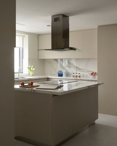 Minimalist kitchen island with veined stone countertop under a glass and steel chimney hood