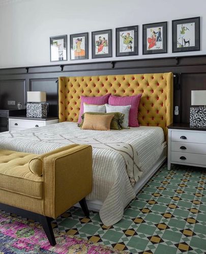 Bedroom with mustard tufted headboard, dark wood paneling, gallery wall, and patterned tile floor