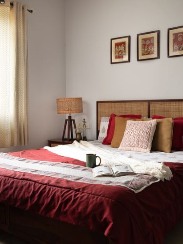 Bed with cane headboard, red linens, patterned cushions, and framed miniature paintings above
