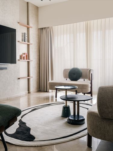 Minimalist living room with beige sofa, round abstract rug, and floating wooden shelves beside a TV