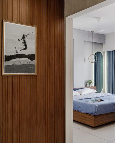 Ribbed wood wall with framed art beside doorway view into bedroom with blue bedding