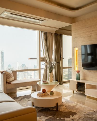 High-rise Mumbai living room with beige furnishings, sculptural tables, and skyline view through floor-to-ceiling windows