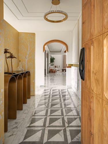Foyer with mustard wallpaper, brass console, carved wood door, and geometric marble floor leading to arched living room