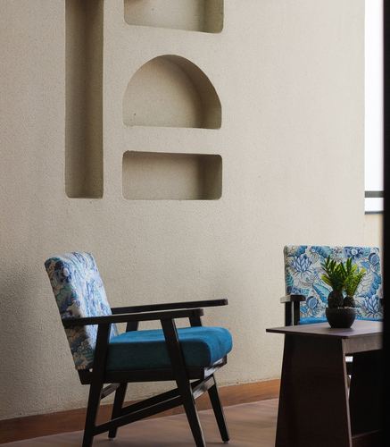 Two floral-blue upholstered armchairs against a plastered wall with arched niches in Udaipur home