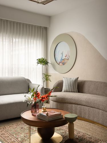 Living room corner with curved boucle sofa, round peacock mirror, and wooden coffee table on a jute rug