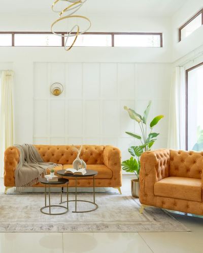 Two orange chesterfield sofas in a white paneled living room with a ring pendant light