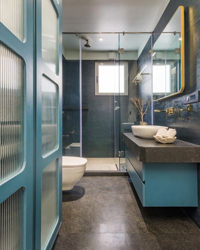 Teal vanity and reeded glass door in a dark stone bathroom with glass shower and arched mirror