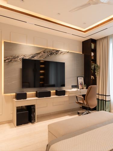 Bedroom TV wall with backlit stone panel, built-in desk, and task chair beside curtained window