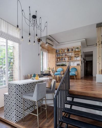 Open-plan kitchen with patterned island, cascading pendant lights, wooden staircase, and living area beyond
