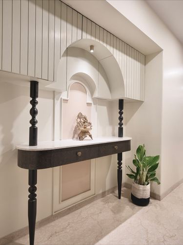 White console table with turned black legs beneath an arched niche holding a brass idol, plant beside it