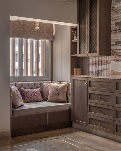 Tufted window seat with patterned cushions beside wood-veneer cabinetry and stone backsplash