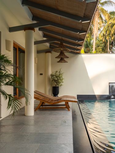 Poolside terrace with wooden loungers, woven pendant lights, and slatted overhang beside infinity pool