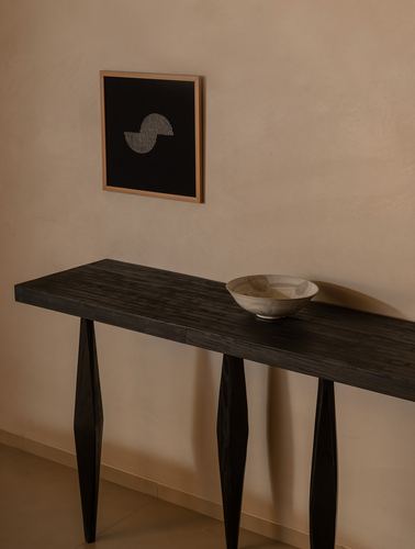 Dark wood console table with ceramic bowl beneath framed abstract artwork on plaster wall