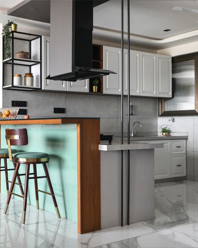 Modern kitchen with white cabinetry, black chimney hood, and a seafoam glass-fronted island with bar stools