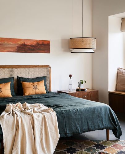 Bedroom with cane headboard, green linen bedding, and a woven pendant light over a wooden nightstand