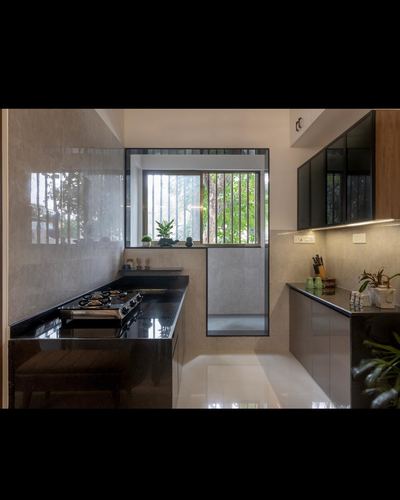 Modern L-shaped kitchen with black countertops, grey stone backsplash, and a window framed by greenery
