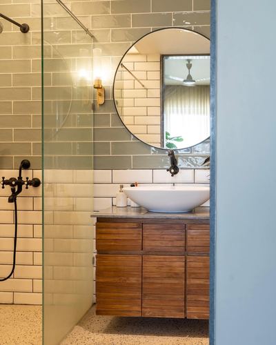 Bathroom vanity with round mirror, vessel sink, wooden cabinetry and subway-tiled shower alcove