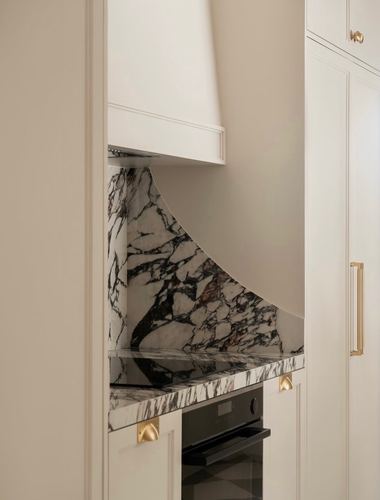 Kitchen detail with curved marble hood, brass hardware, and paneled cream cabinetry