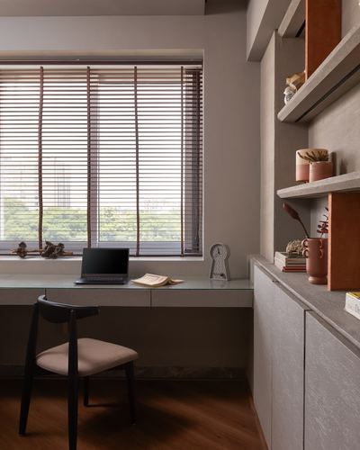 Study nook with glass desk, laptop, and windows beside a textured stone shelf unit