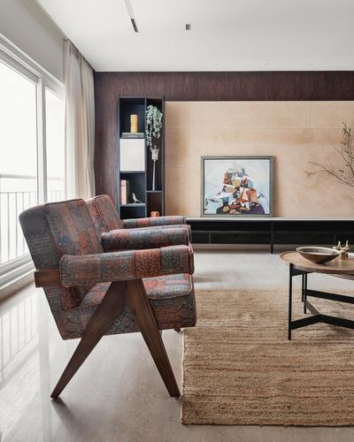 Living room corner with patterned lounge chair, dark wood shelf, and abstract painting on stone wall