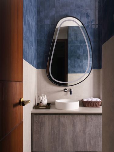 Powder room with blue tiled wall, organic mirror, and round vessel sink on stone counter