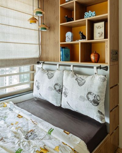 Child's bedroom window seat bed with printed bedding under wooden shelving and pendant lights