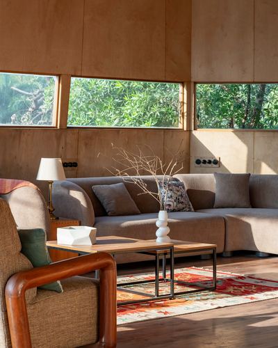 Wood-paneled living room with sectional sofa, coffee table, and horizontal windows onto greenery