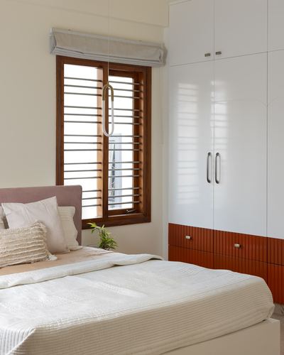 Bedroom corner with arched white wardrobe, orange drawers, wooden louvered window and pink upholstered bed