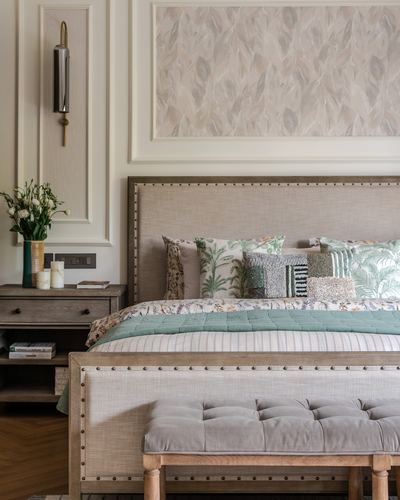 Neutral bedroom with upholstered nailhead headboard, patterned pillows, and paneled wall with wallpaper insert
