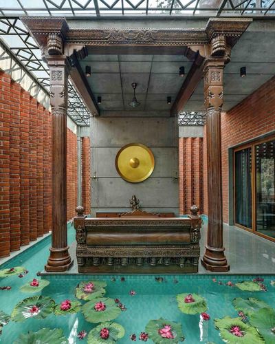 Carved wooden pergola with bench over a lotus pond framed by exposed brick walls