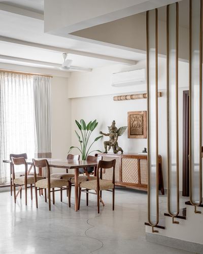 Dining area with wooden table and chairs beside a cane sideboard, brass staircase railings in foreground