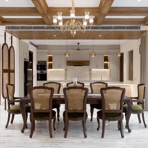 Formal dining room with cane-back chairs, chandelier, coffered wood ceiling, open kitchen beyond