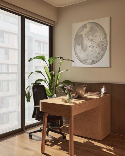 Wooden desk with laptop and moon artwork beside a floor-to-ceiling window