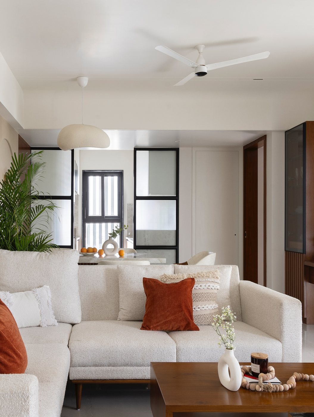 Cream boucle sectional with rust cushions in a living room opening to dining area behind glass partition