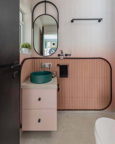 Pink ribbed tile bathroom with black oval mirror and green vessel sink on pink vanity