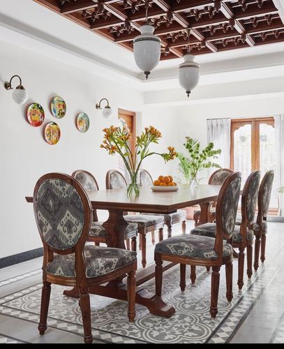 Dining room with carved wood coffered ceiling, ikat-upholstered chairs, and decorative wall plates