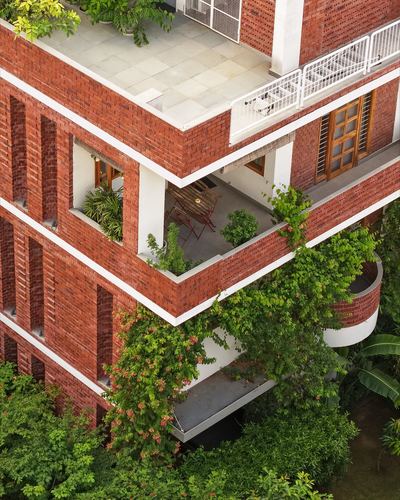 Aerial angled view of a red brick building with recessed balconies, plants, and climbing vines